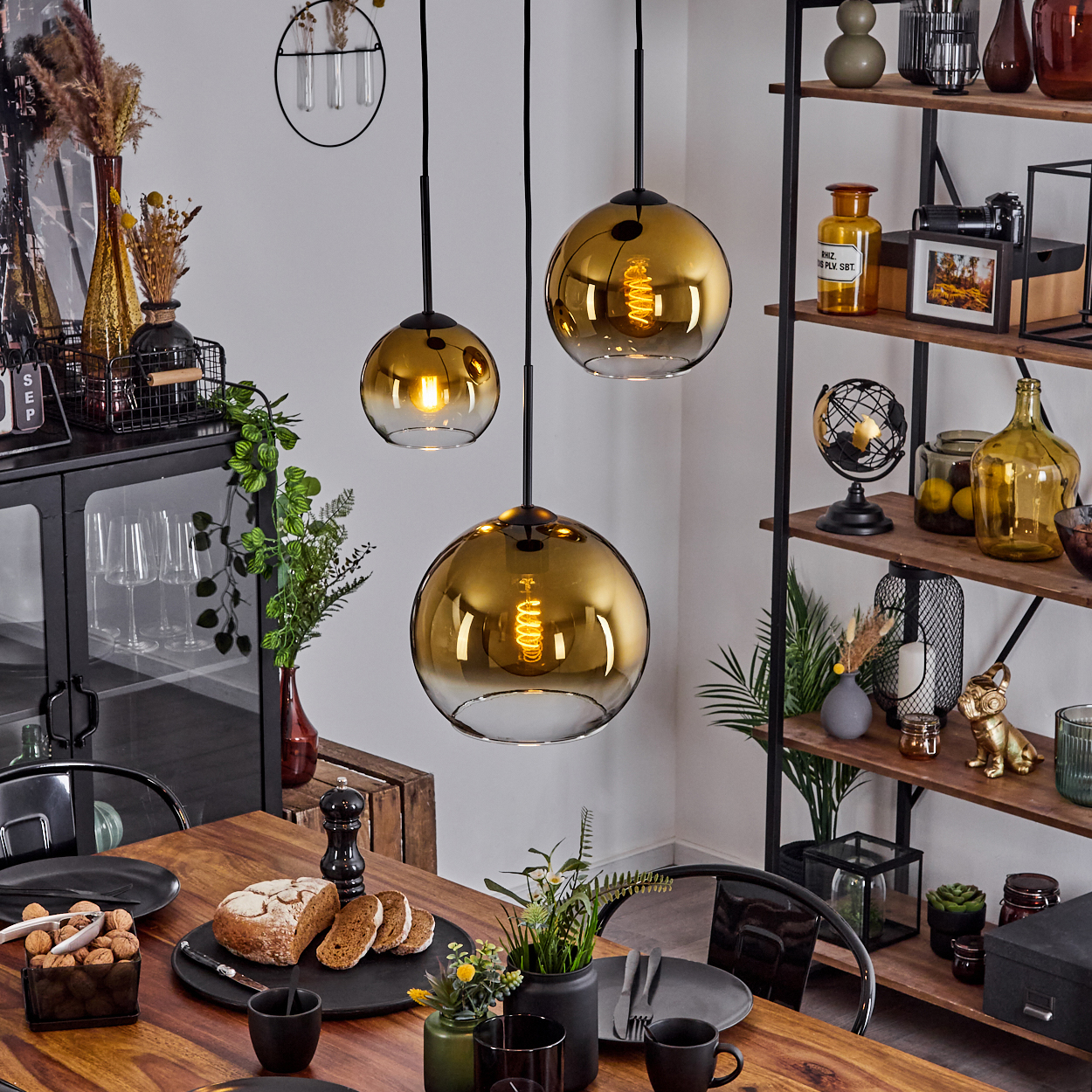 Esszimmer mit Holztisch, goldenen Pendelleuchten, Regalen mit Dekoration, Brot und Tellern.