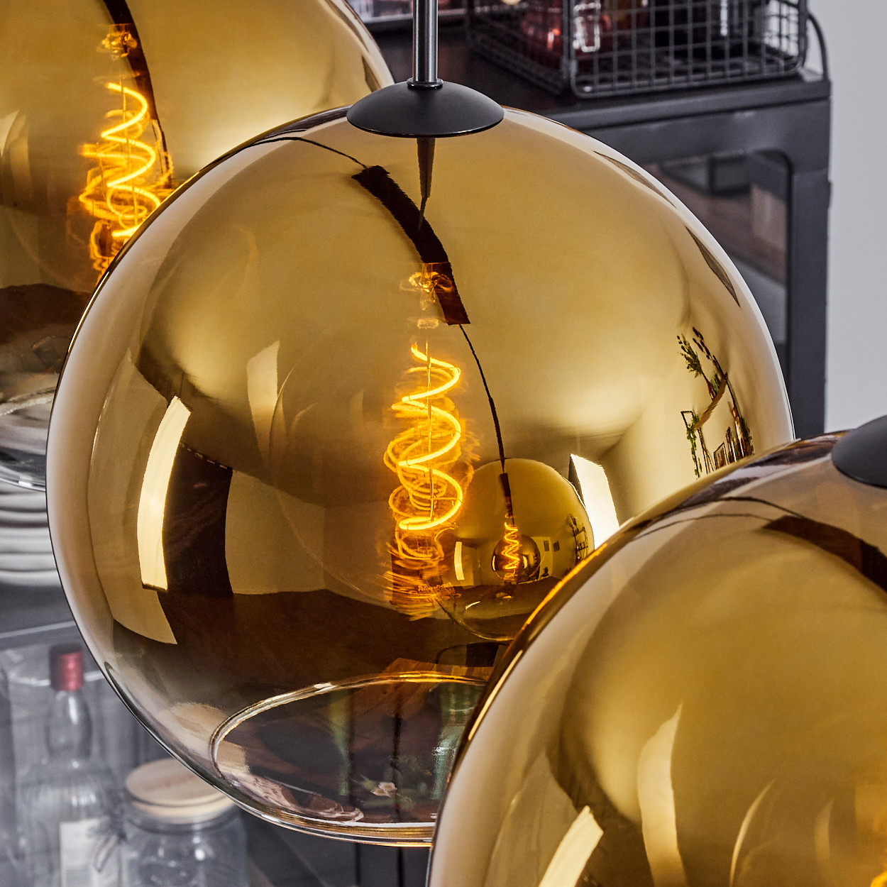 Nahaufnahme von drei goldenen Kugellampen. Jede hat ein spiralförmiges Glühfaden. Der Hintergrund zeigt eine unscharfe Küchenumgebung.