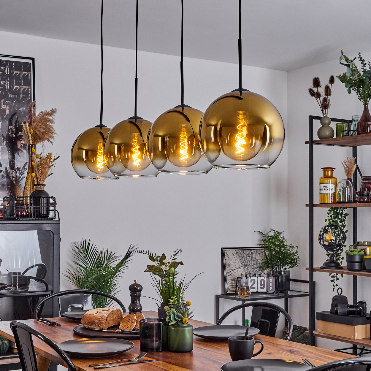 Esszimmer mit Holztisch, schwarzen Stühlen und fünf hängenden goldenen Pendelleuchten. Tisch mit Tellern und Essen gedeckt.