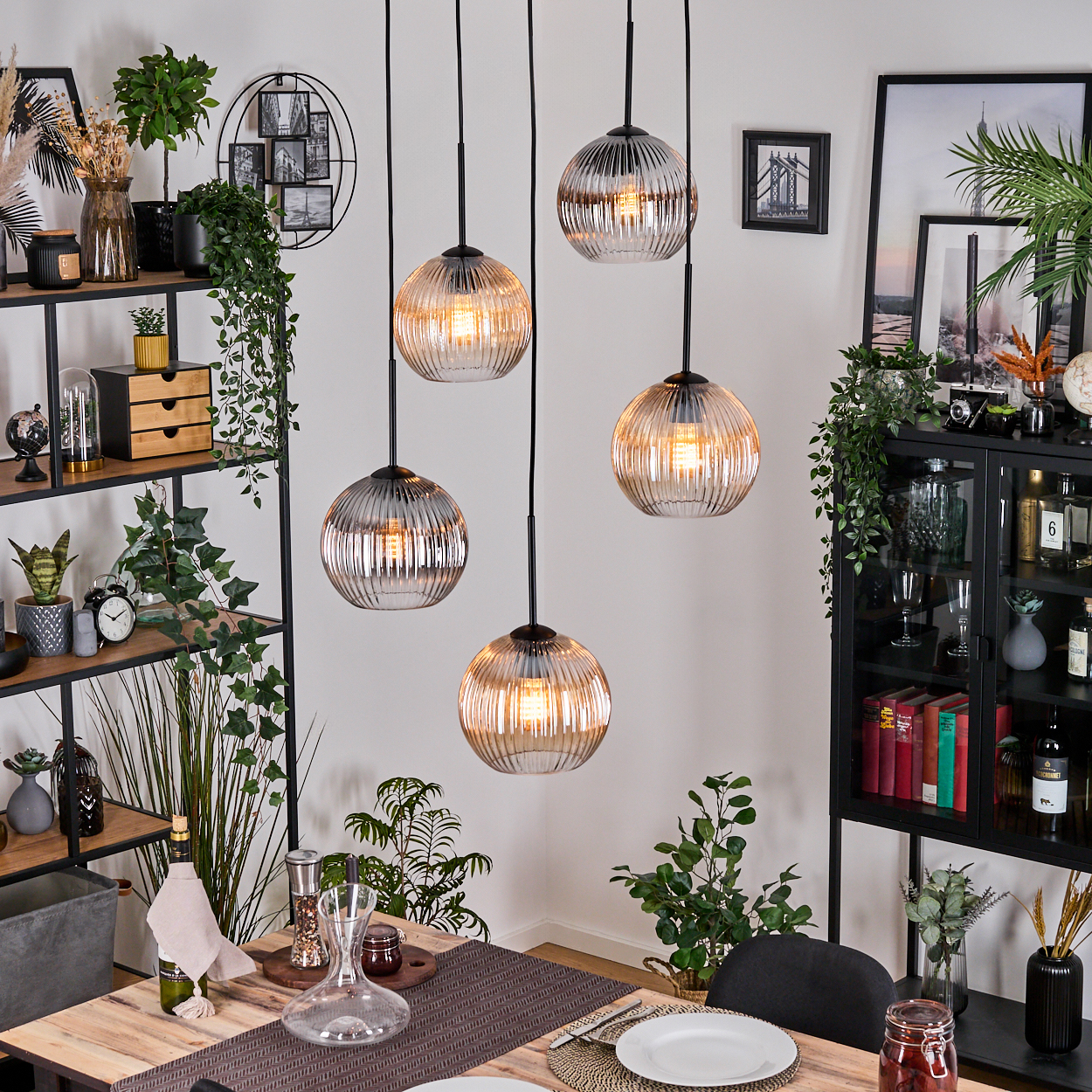 Esszimmer mit Hängelampen. Tisch mit Tellern und einer Weinkaraffe. Pflanzen und Dekorationsartikel sind vorhanden.