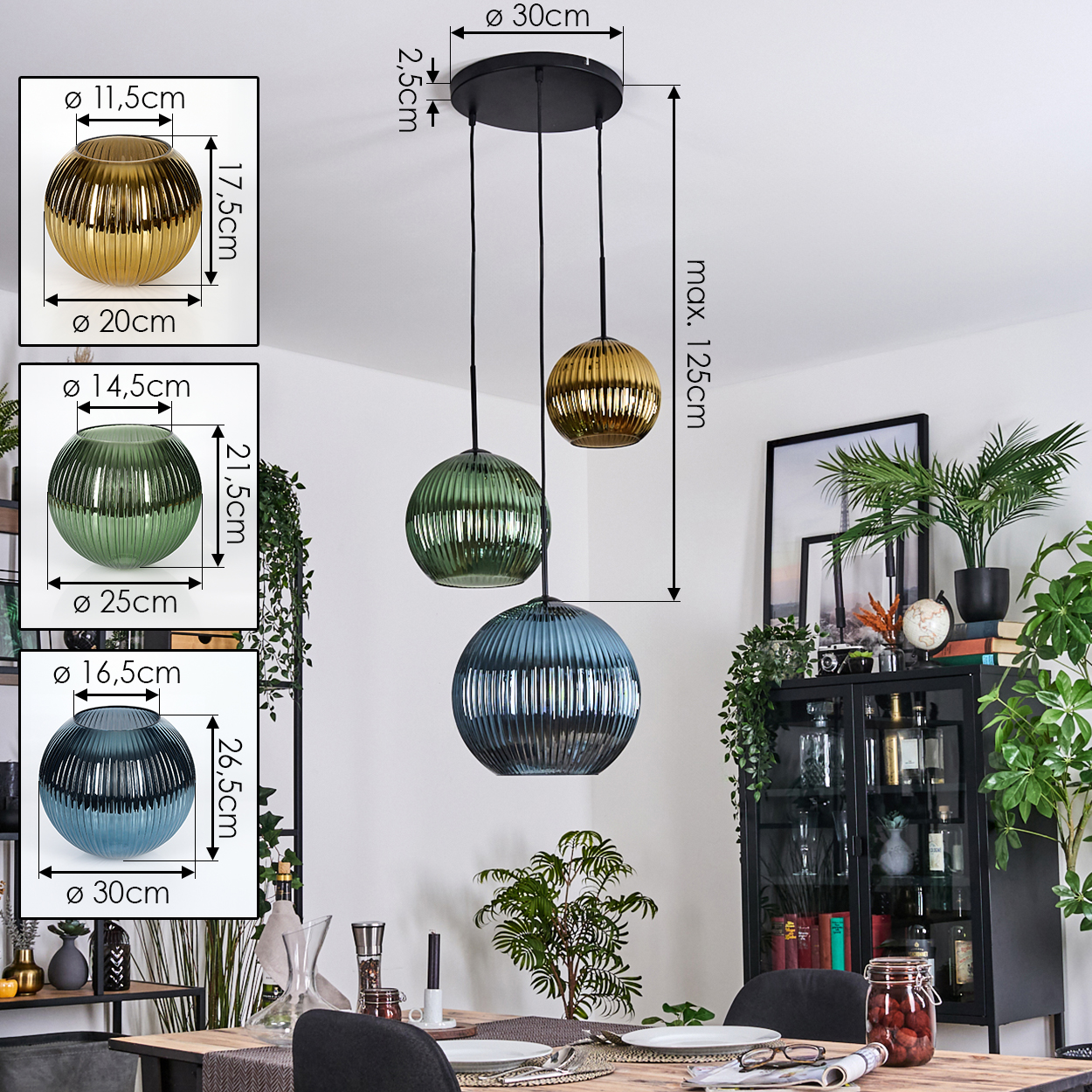Drei Pendelleuchten mit Glaskugeln in Gold, Grün und Blau hängen über einem Esstisch. Im Hintergrund ein Schrank und Pflanzen.