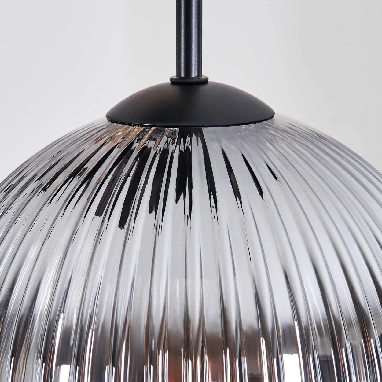 Nahaufnahme einer Glas-Pendelleuchte mit geripptem Design. Die Leuchte hat einen schwarzen Metallaufsatz und einen klaren, reflektierenden Glasschirm.