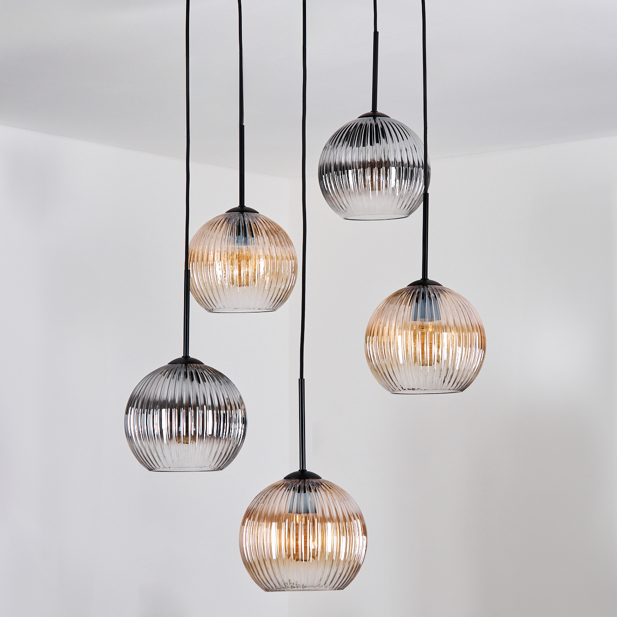 Fünf Pendelleuchten aus Glas hängen von der Decke. Die Kugeln sind gerippt und haben warmes Licht im Inneren, mit schwarzen Kabeln.