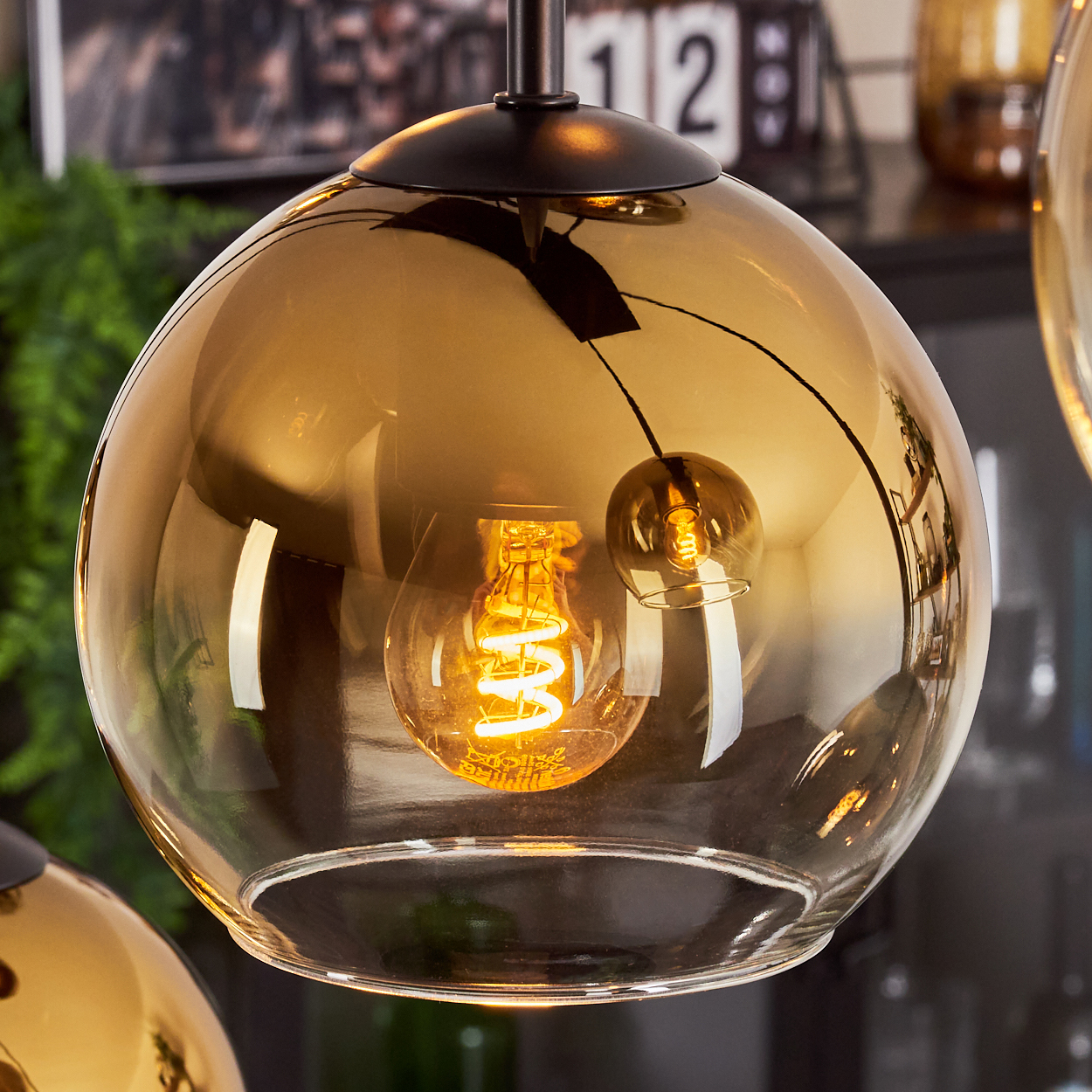 Nahaufnahme einer Glashängeleuchte mit warmer Glühbirne. Die Kugel ist bernsteinfarben und reflektiert die Umgebung.