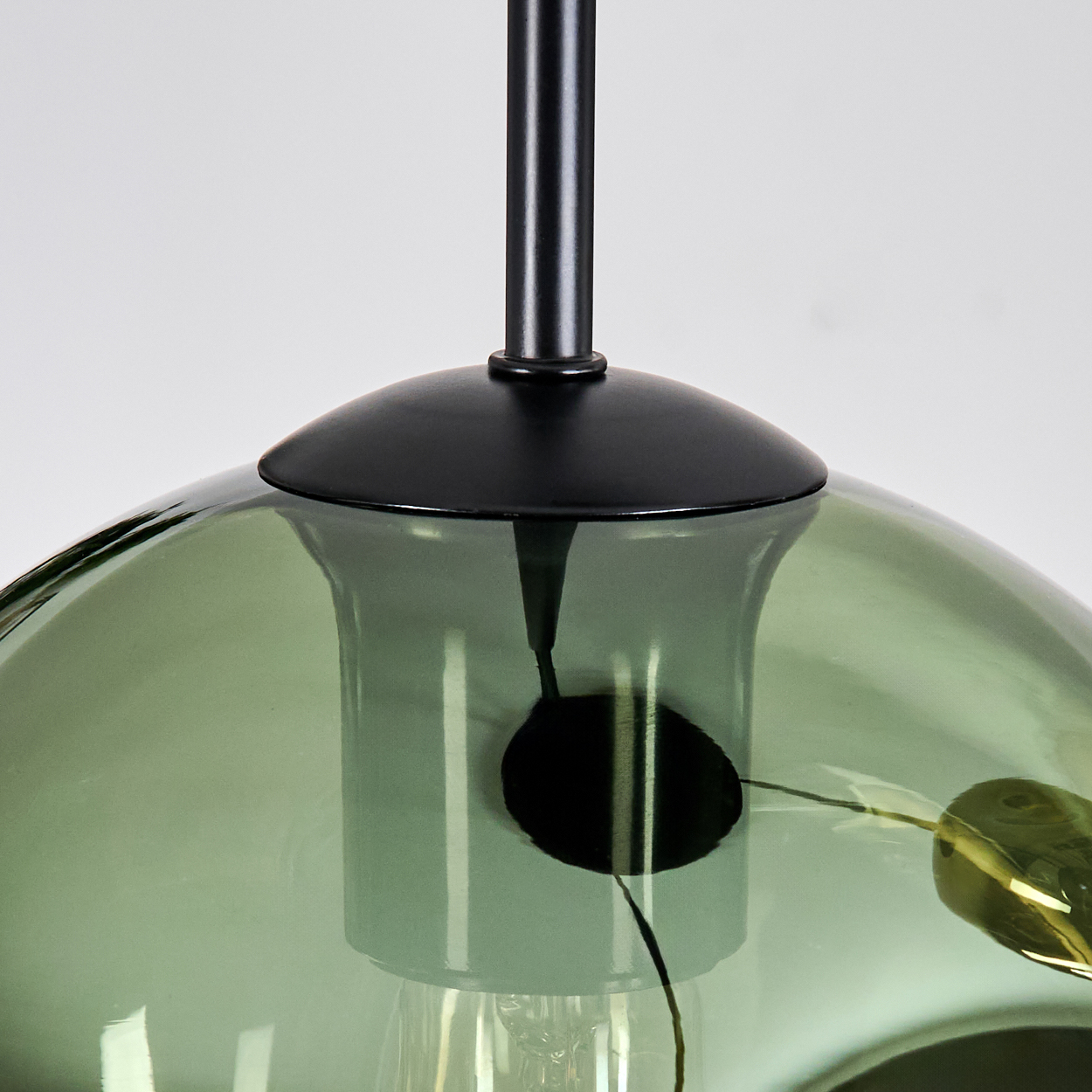 Nahaufnahme einer grünen Glas-Hängelampe mit schwarzem Stiel und Halterung, vor weißem Hintergrund aufgehängt.