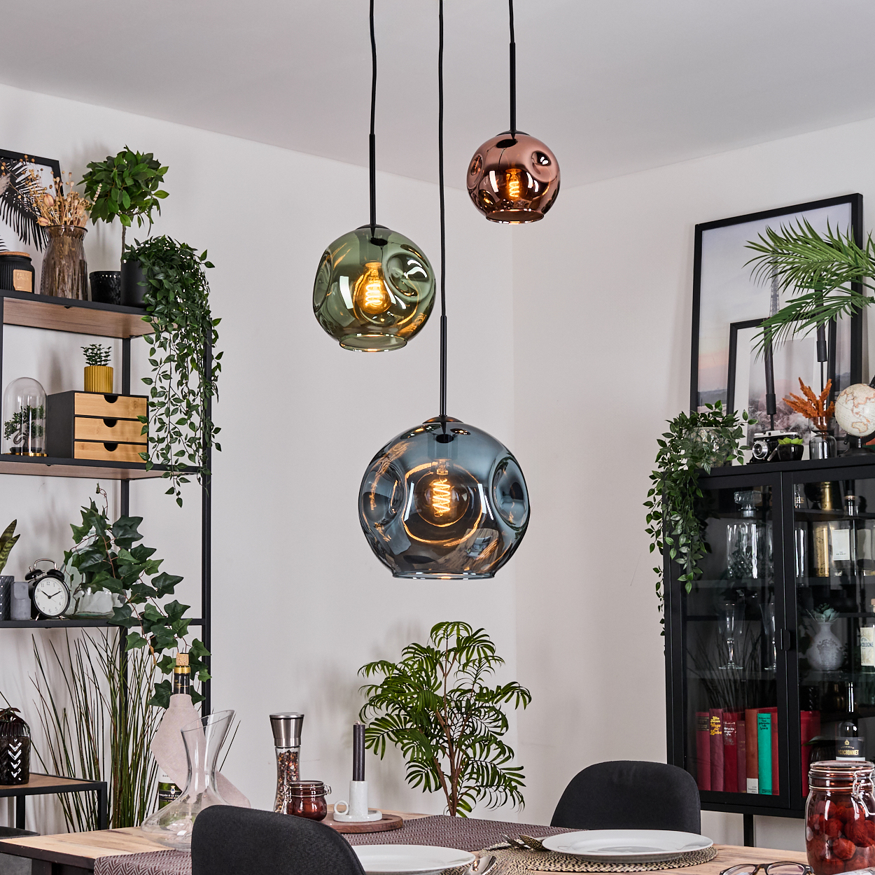 Esszimmer mit drei kugelförmigen Pendelleuchten. Pflanzen und Regale mit dekorativen Gegenständen sind sichtbar.