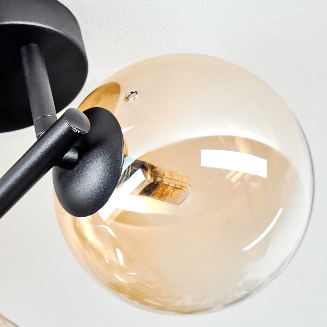 Nahaufnahme einer modernen Leuchte. Sie hat einen schwarzen Metallrahmen und eine große, bernsteinfarbene Glaskugel.