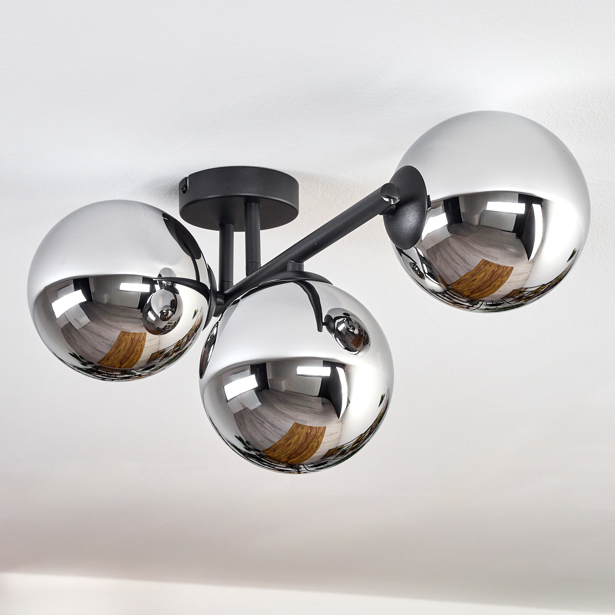 Moderne Deckenleuchte mit drei reflektierenden Chromkugeln. Die Kugeln reflektieren den Raum, montiert auf schwarzen Armen und einem schwarzen Sockel.