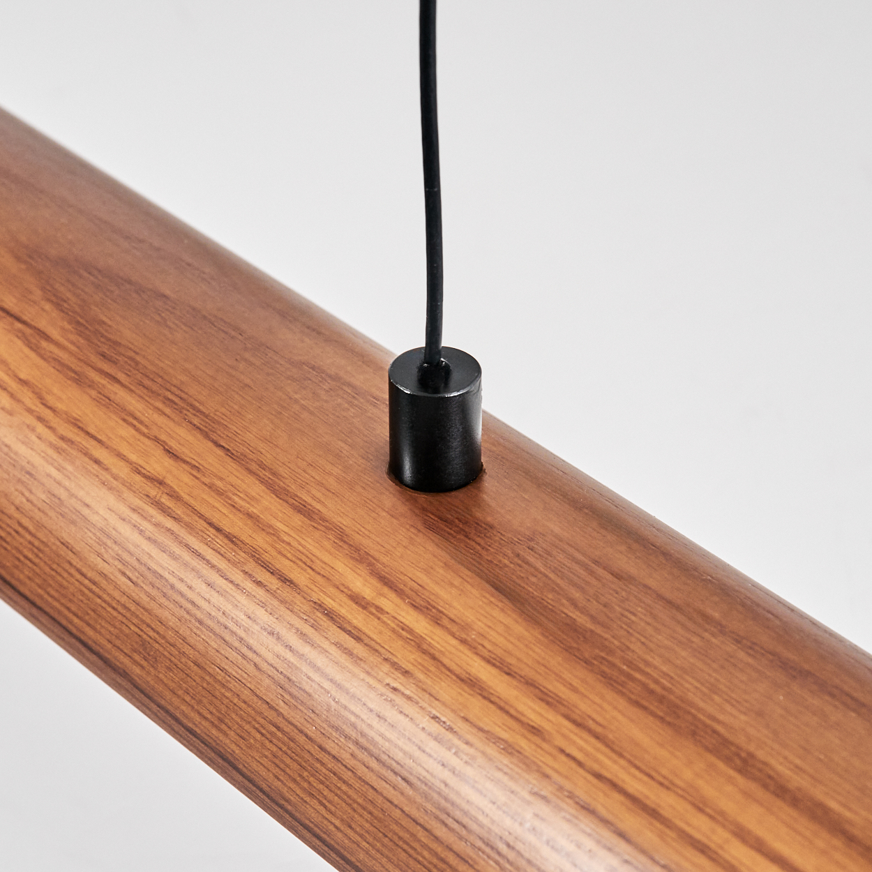 Nahaufnahme eines Holzbalkens mit einem schwarzen Zylinder und einem schwarzen Kabel, das von oben vor weißem Hintergrund hängt.