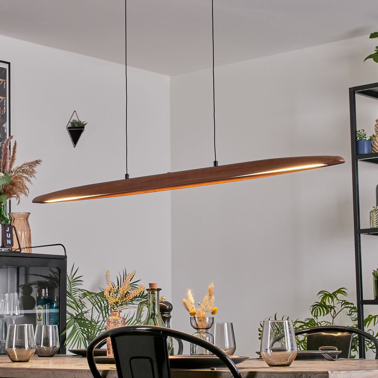Ein modernes Esszimmer mit einer beleuchteten Holzleuchte über dem Tisch. Pflanzen und Gläser stehen auf dem Tisch.