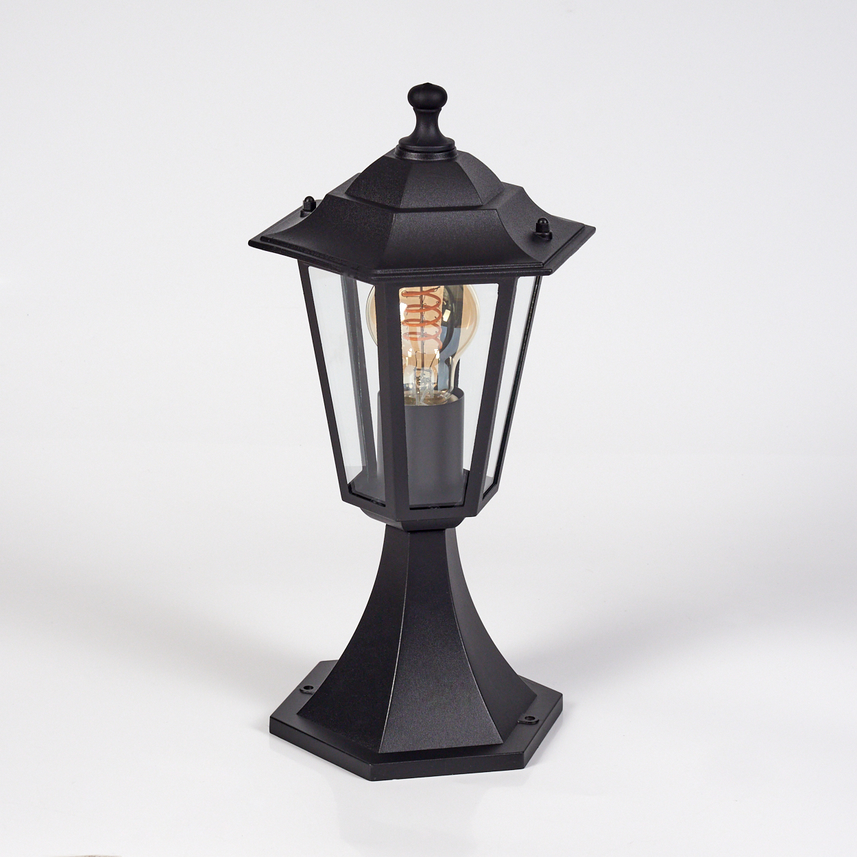 Eine schwarze Außenlampe mit Glasgehäuse und Glühbirne, die auf einer weißen Oberfläche steht.