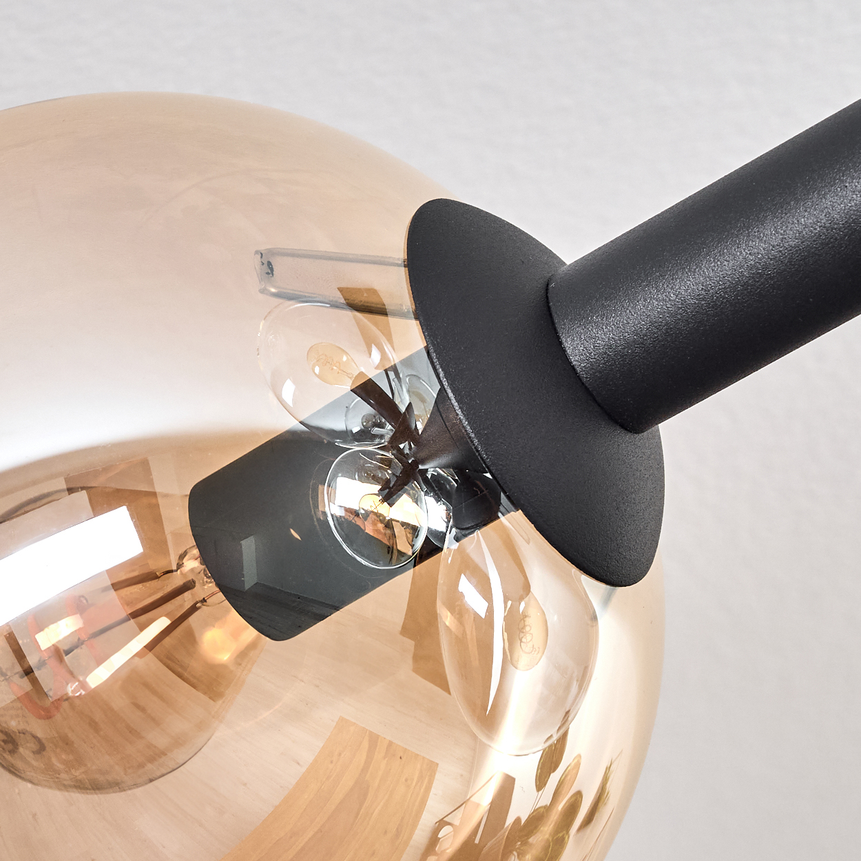 Nahaufnahme einer Lampe mit schwarzem Arm und brauner Glaskugel mit Glühbirnen. Der Hintergrund ist weiß.