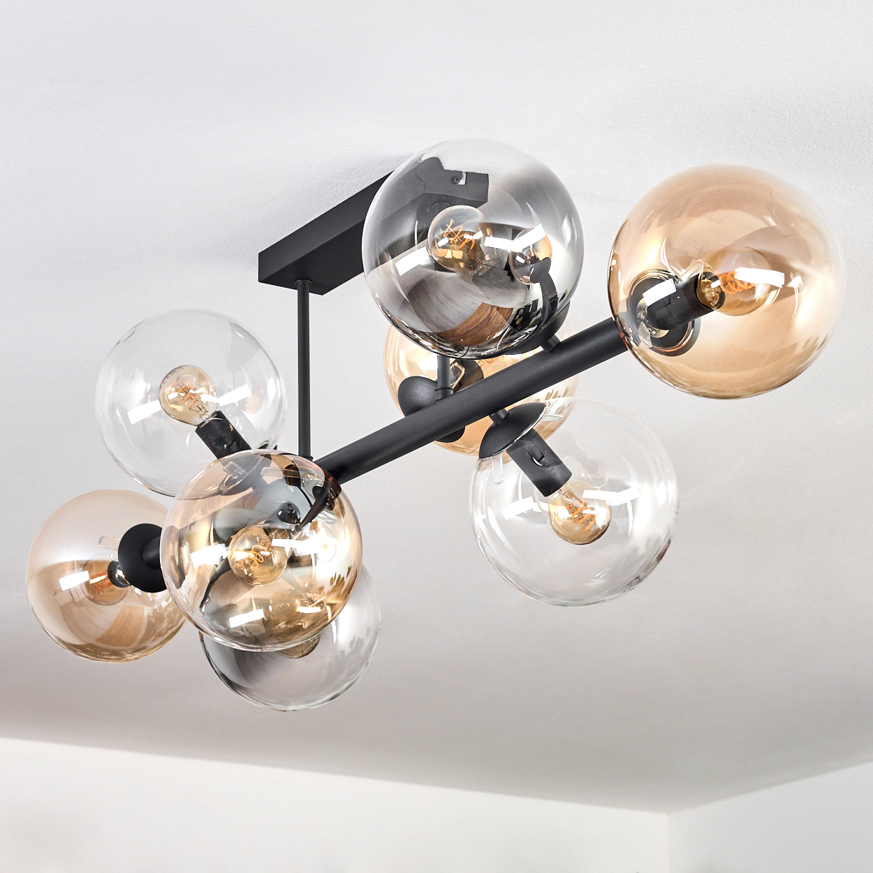 Eine moderne Deckenleuchte mit kugelförmigen Glasschirmen in klar und bernsteinfarben. Schwarze Metallarme halten die Glühbirnen.