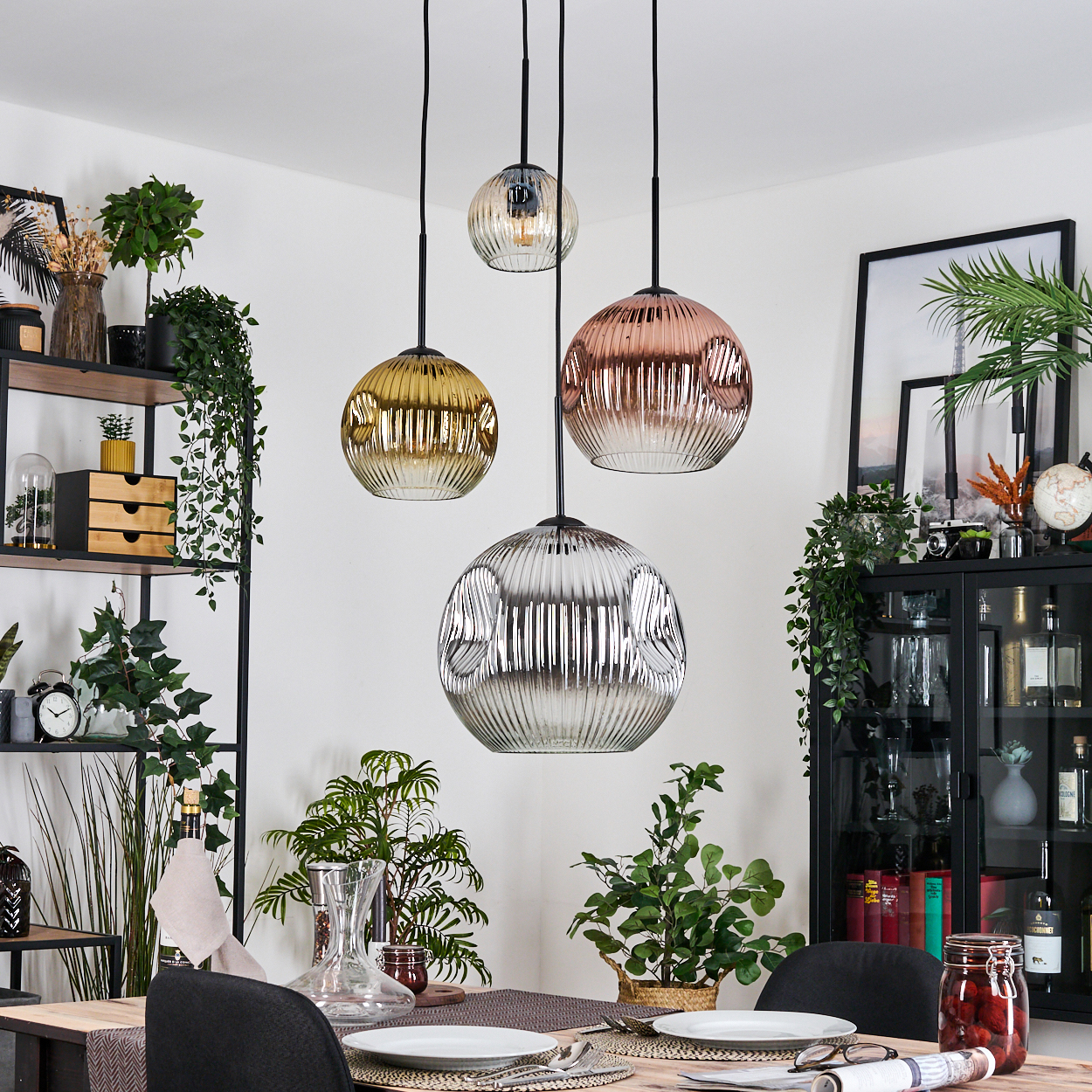 Esszimmer mit Hängekugelleuchten, gedecktem Tisch, Pflanzen und einem schwarzen Schrank mit verschiedenen Gegenständen.