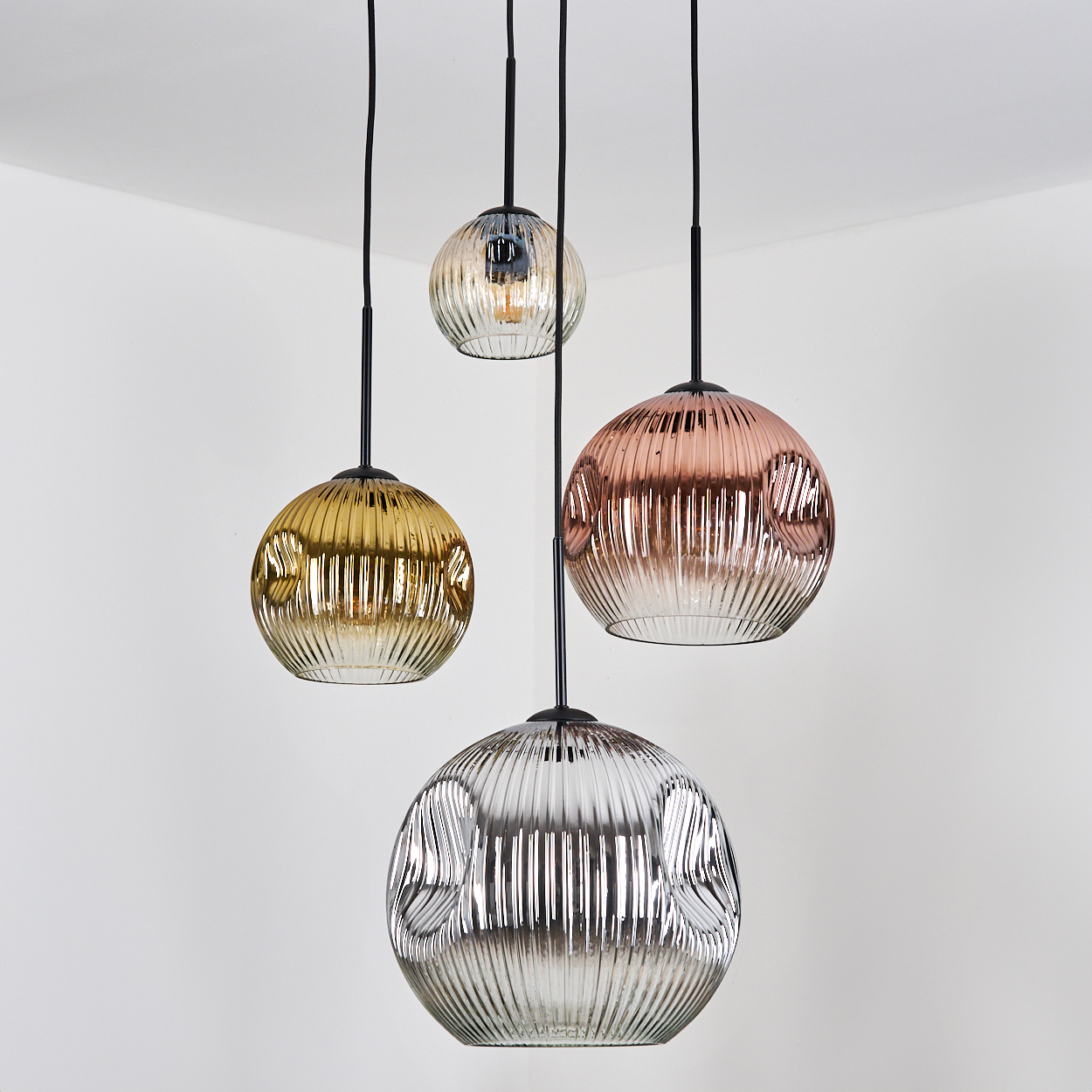 Vier kugelförmige Pendelleuchten mit strukturierten Glasschirmen. Farben variieren: Gold, Rose, klar und Silber. Schwarze Kabel hängen von der Decke.
