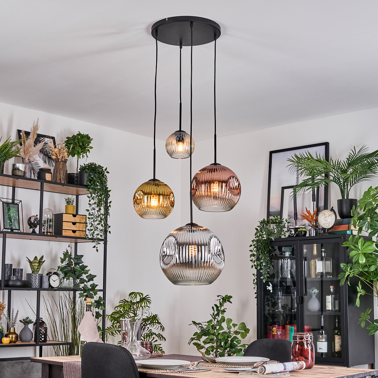 Esszimmer mit Hängelampen, Pflanzen und einem schwarzen Schrank. Der Tisch ist gedeckt. Lampen sind Glaskugeln in Bernstein und Silber.