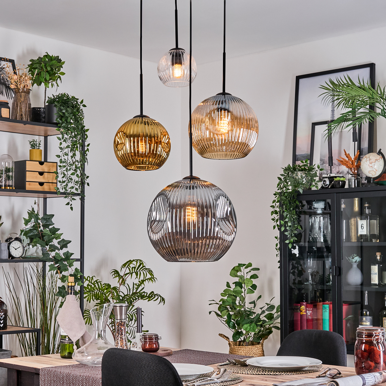 Esszimmer mit drei Hängelampen. Pflanzen, Holztisch, schwarze Stühle und ein schwarzer Schrank mit Glastüren.