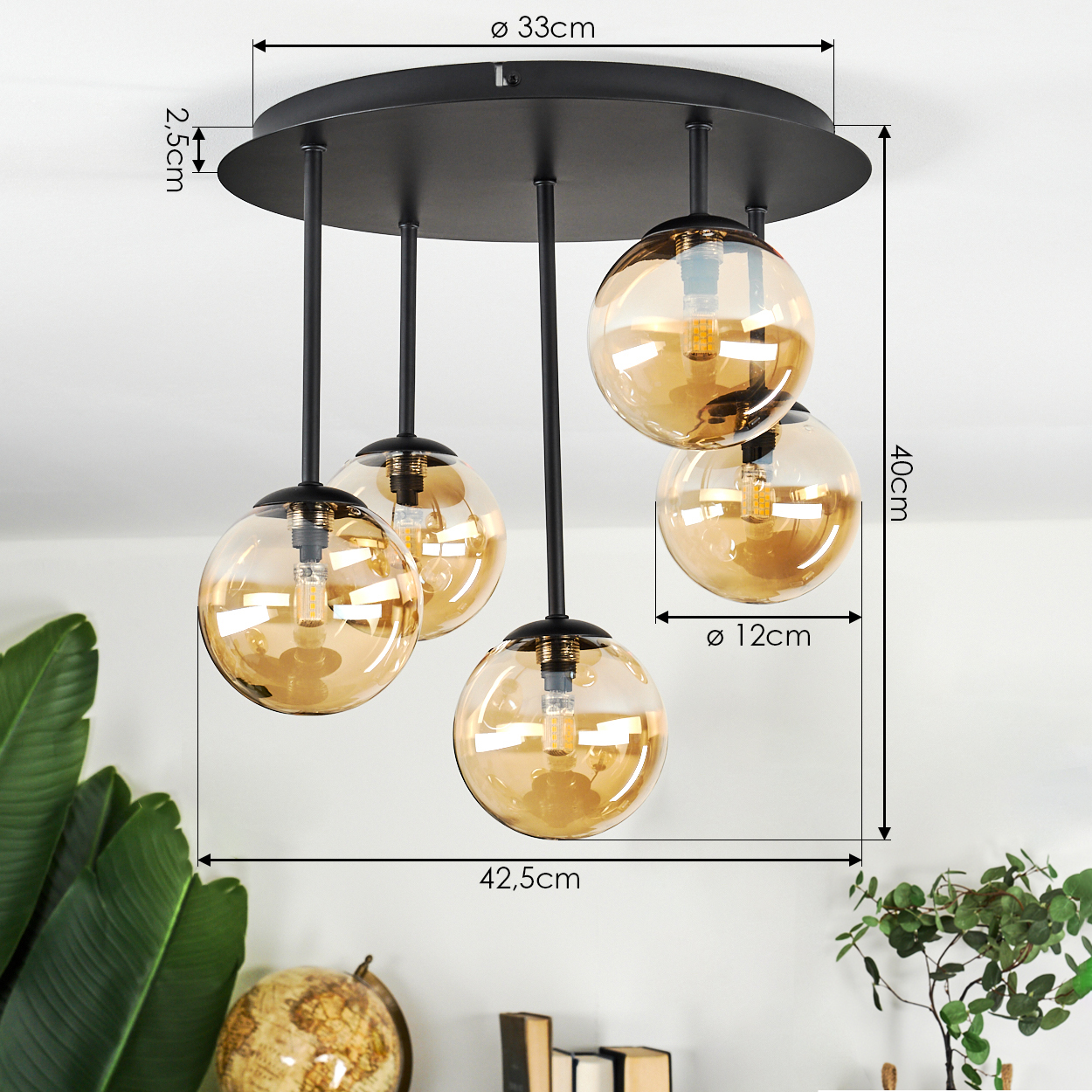 Moderne schwarze Deckenlampe mit fünf bernsteinfarbenen Glaskugeln. Maße in Zentimetern. Pflanzen und ein Globus im Hintergrund.