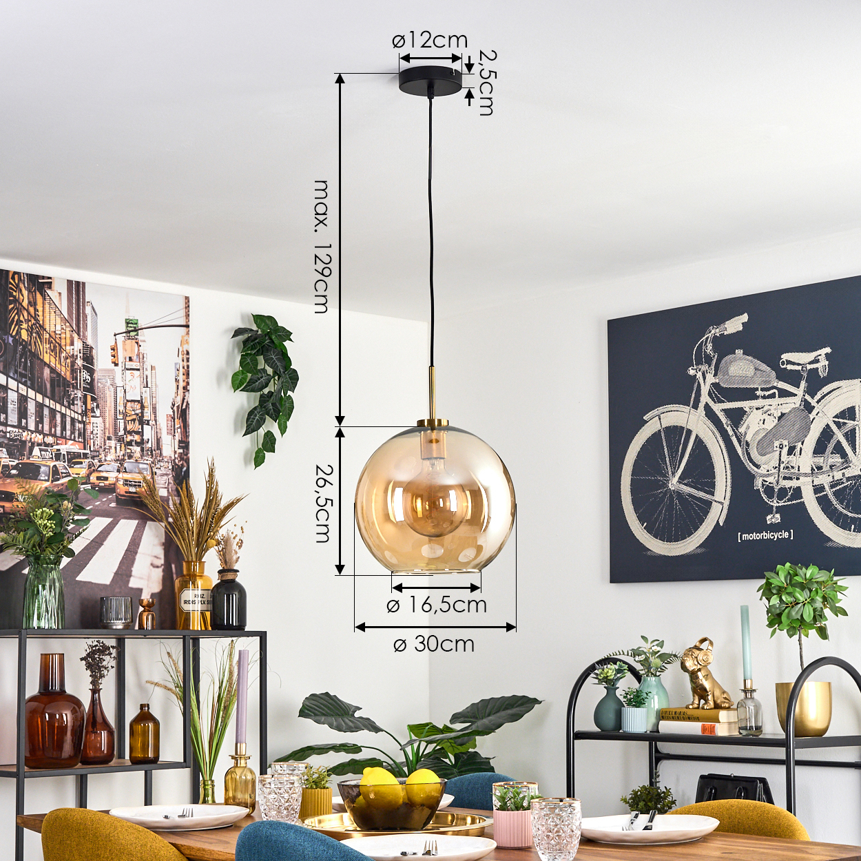 Eine Pendelleuchte mit goldener Kugel hängt über einem Holztisch. Abmessungen sind beschriftet. Hintergrund zeigt Kunst, Pflanzen und Esstisch.