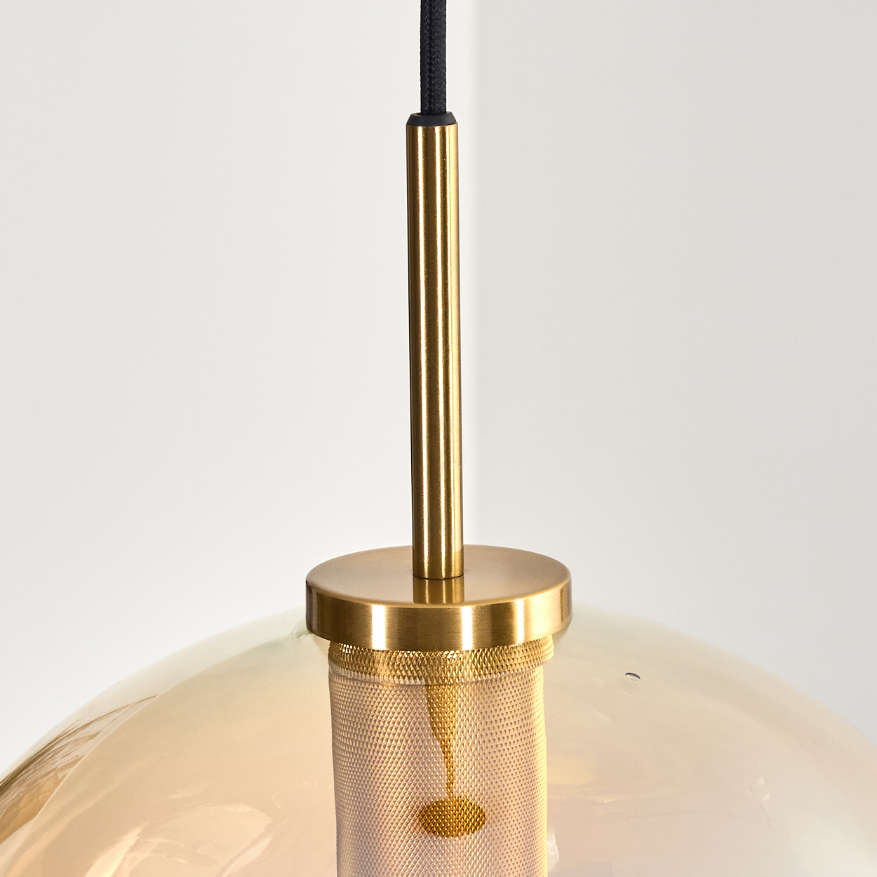 Nahaufnahme einer modernen Pendelleuchte. Sie hat einen goldfarbenen Metallrahmen mit einem Netz und einem transparenten, bernsteinfarbenen Glasschirm.
