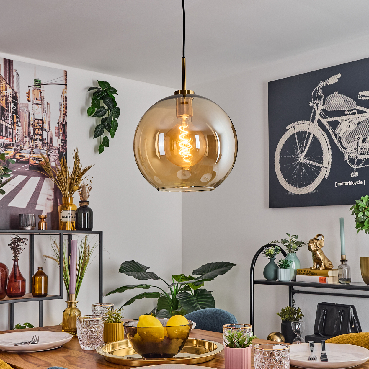 Ein Esszimmer mit einer großen, bernsteinfarbenen Glashängelampe. Ein Tisch ist mit Tellern, Gläsern und einer Schüssel mit Zitronen gedeckt.