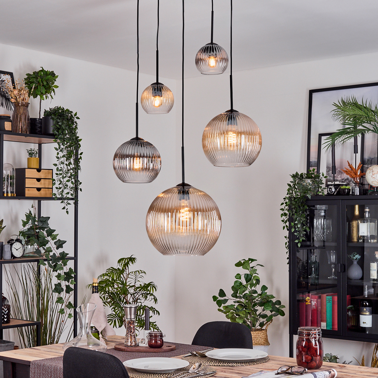 Esszimmer mit hängenden Glaslampen. Tisch zum Abendessen gedeckt, Schränke mit Pflanzen und Dekorationen. Grüne Pflanzen sichtbar.