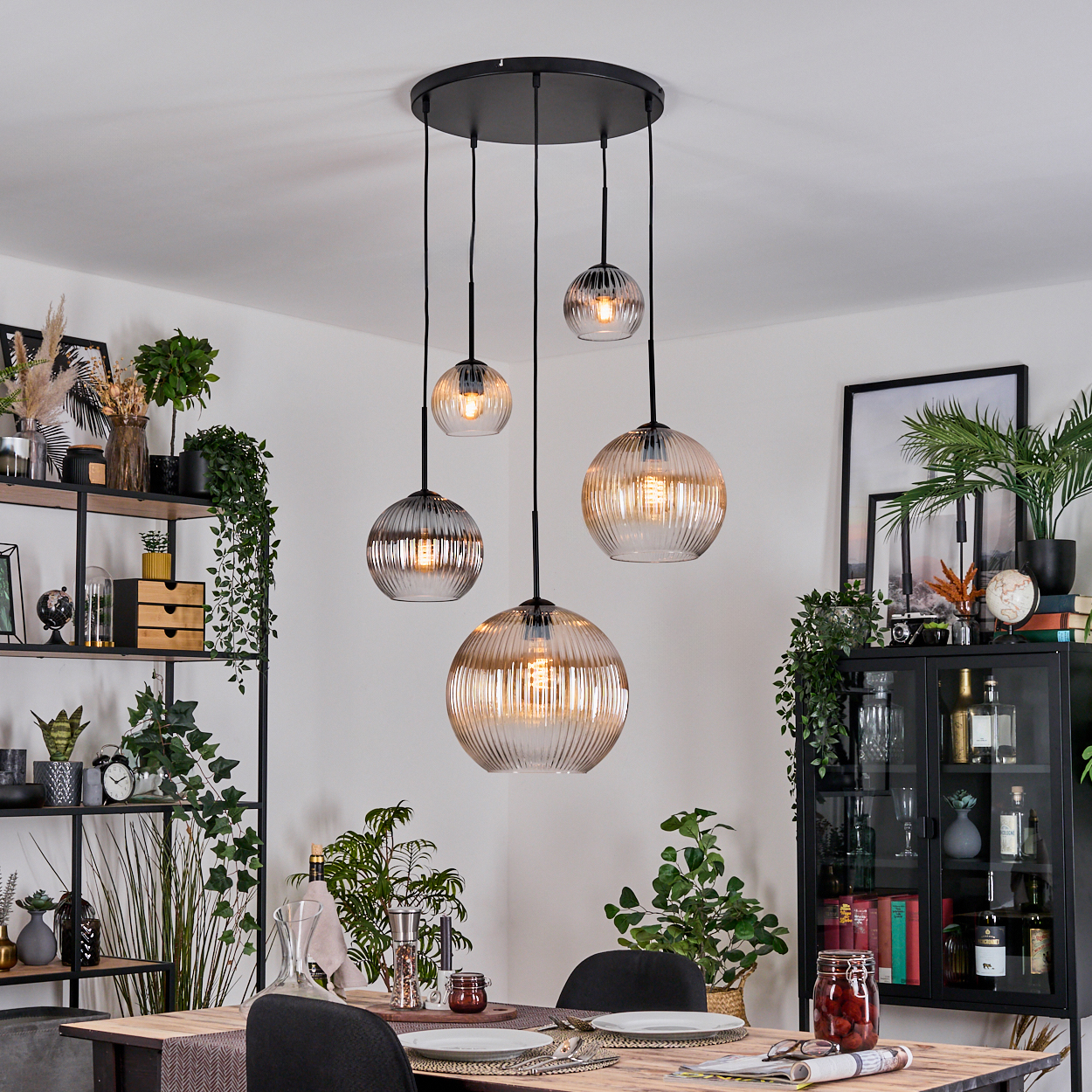 Esszimmer mit Holztisch, Stühlen und Hängeleuchten. Regale und ein Schrank sind mit Pflanzen und Dekor sichtbar.