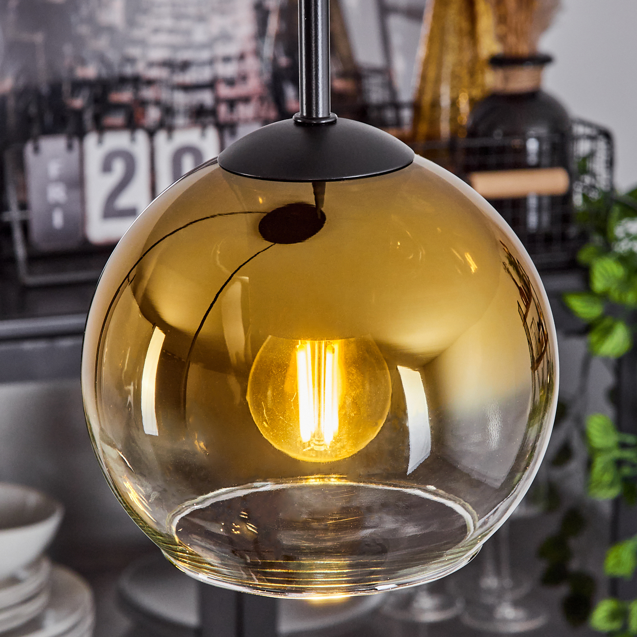 Nahaufnahme einer Pendelleuchte mit goldener Glaskugel. Darin ist eine leuchtende Glühbirne zu sehen. Die Lampe hängt an einer schwarzen Halterung.