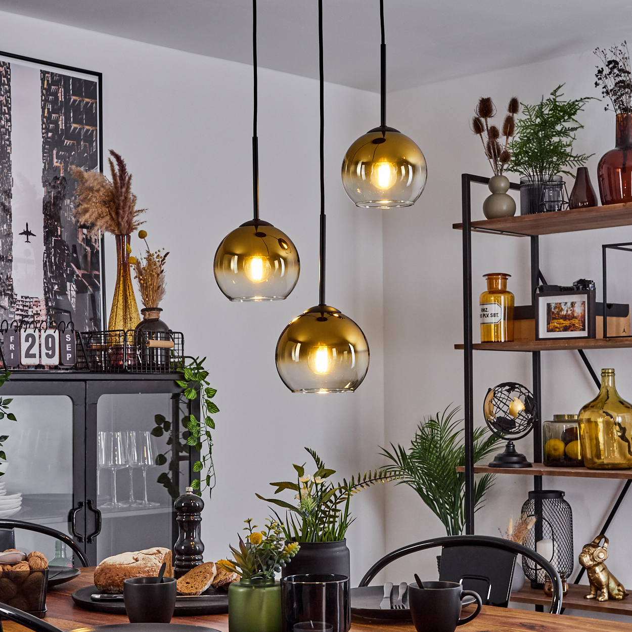 Esszimmer mit Hängelampen. Tisch mit Essen und Tassen gedeckt. Regale im Hintergrund mit Dekorationen.