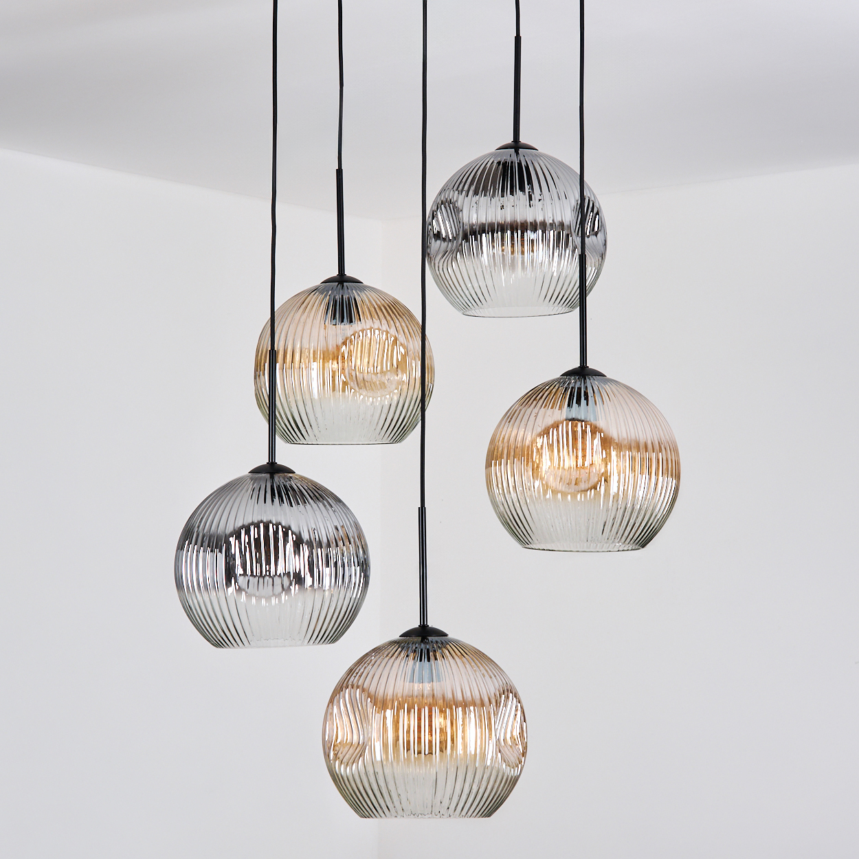 Fünf Glas-Kugel-Pendelleuchten hängen an schwarzen Kabeln vor weißem Hintergrund. Die Kugeln haben ein geripptes Design.