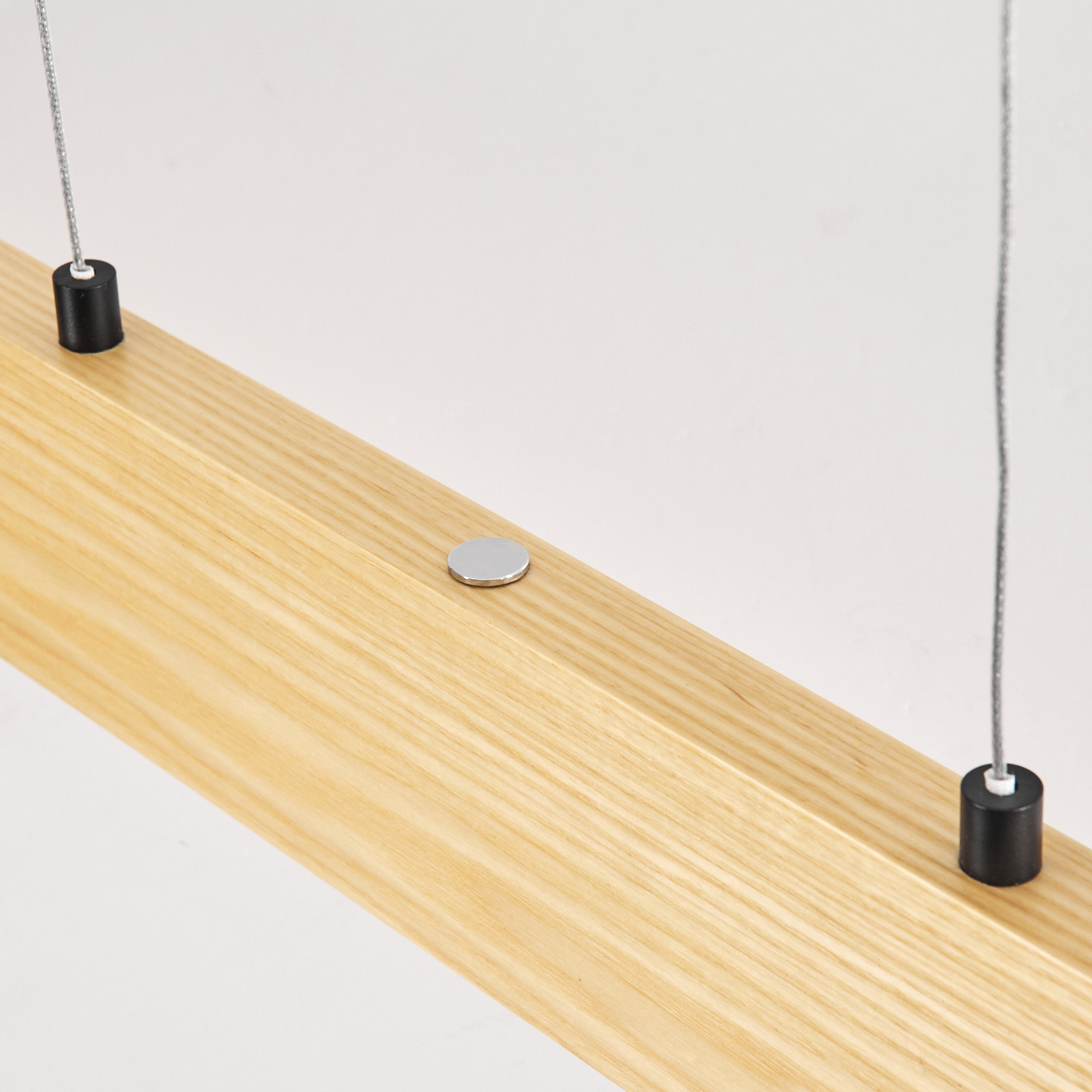 Holzbalken mit Metallscheibe und schwarzen Zylindern, die an Drähten vor weißem Hintergrund hängen.