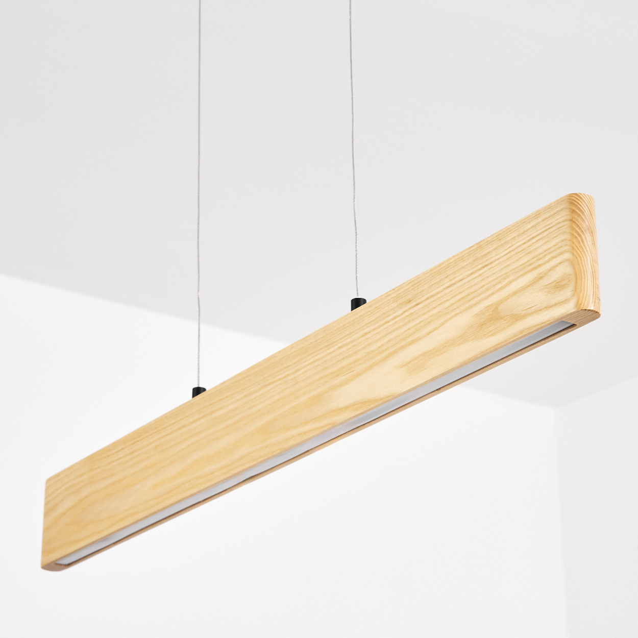 Eine rechteckige Holzleuchte hängt von der Decke. Sie hat einen Lichtstreifen und wird von dünnen Kabeln gehalten.
