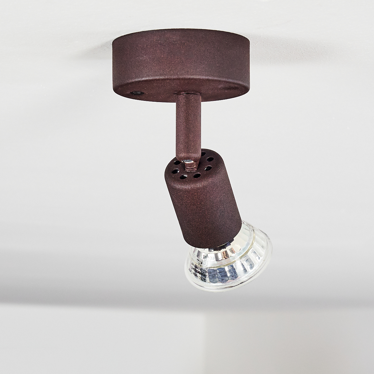 Eine braune Scheinwerferbefestigung ist an einer weißen Decke montiert. Die Lampe ist nach unten geneigt, mit einer klaren Glühbirne.