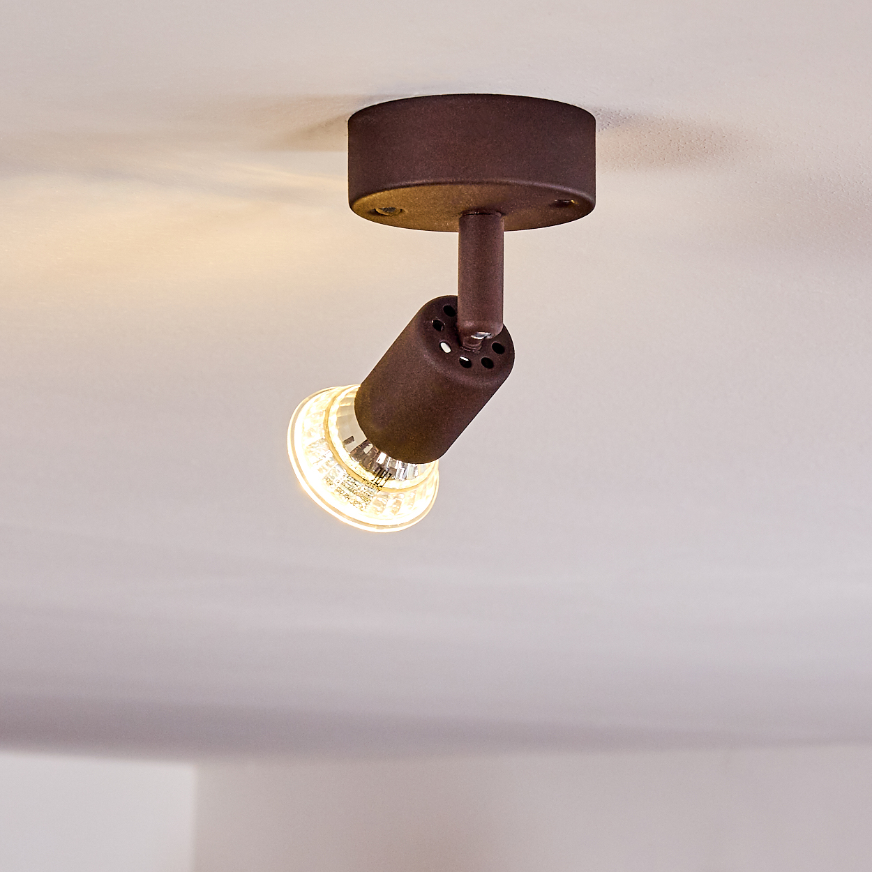 Eine braune Strahlerbefestigung ist an einer weißen Decke angebracht. Das Licht ist an und beleuchtet den Raum darunter.