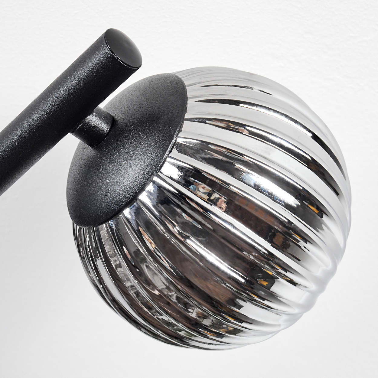 Nahaufnahme einer Lampe mit schwarzem Arm und silbernem, geripptem, kugelförmigem Lampenschirm vor weißem Hintergrund.