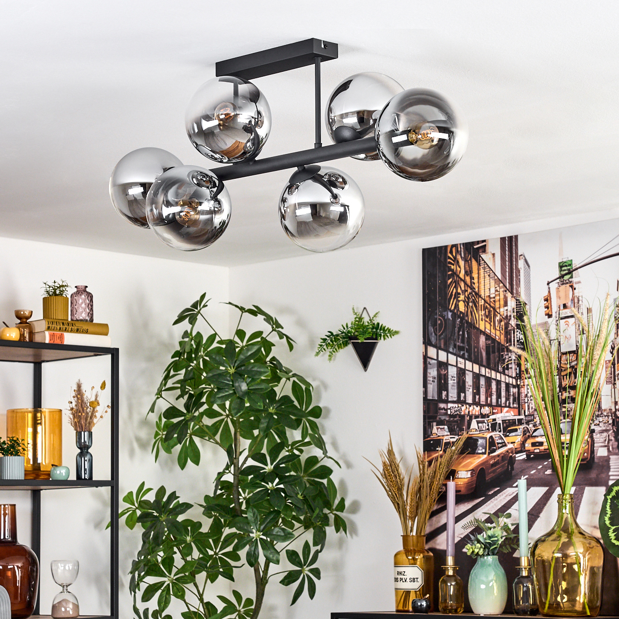 Ein modernes Wohnzimmer mit einem schwarzen Kronleuchter mit Glaskugeln, einer großen Pflanze und einem Stadtbildgemälde.