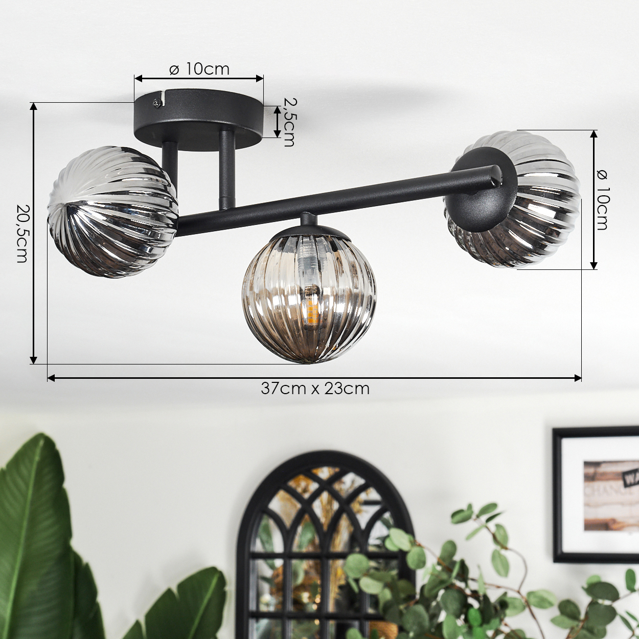 Moderne Deckenlampe mit drei Glaskugeln, schwarzer Rahmen. Abmessungen werden angezeigt. Vordergrund: Pflanzen, Wanddekor.