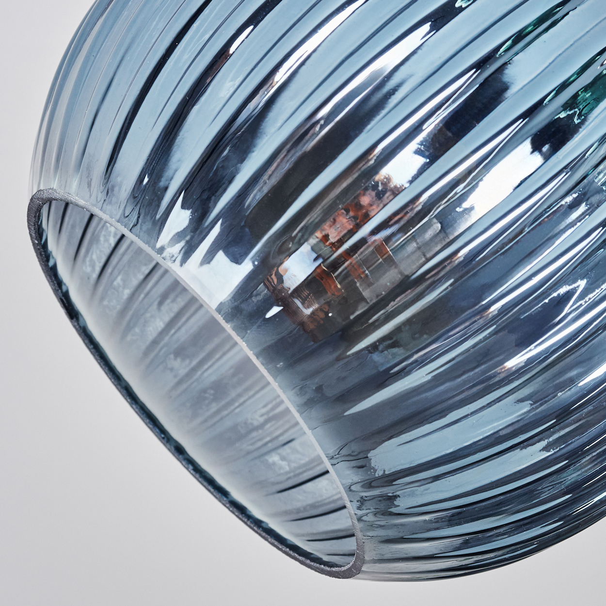 Nahaufnahme eines blauen Glaslampenschirms mit gerippter Textur, der Licht reflektiert. Die Glühbirne ist im Inneren vor weißem Hintergrund sichtbar.