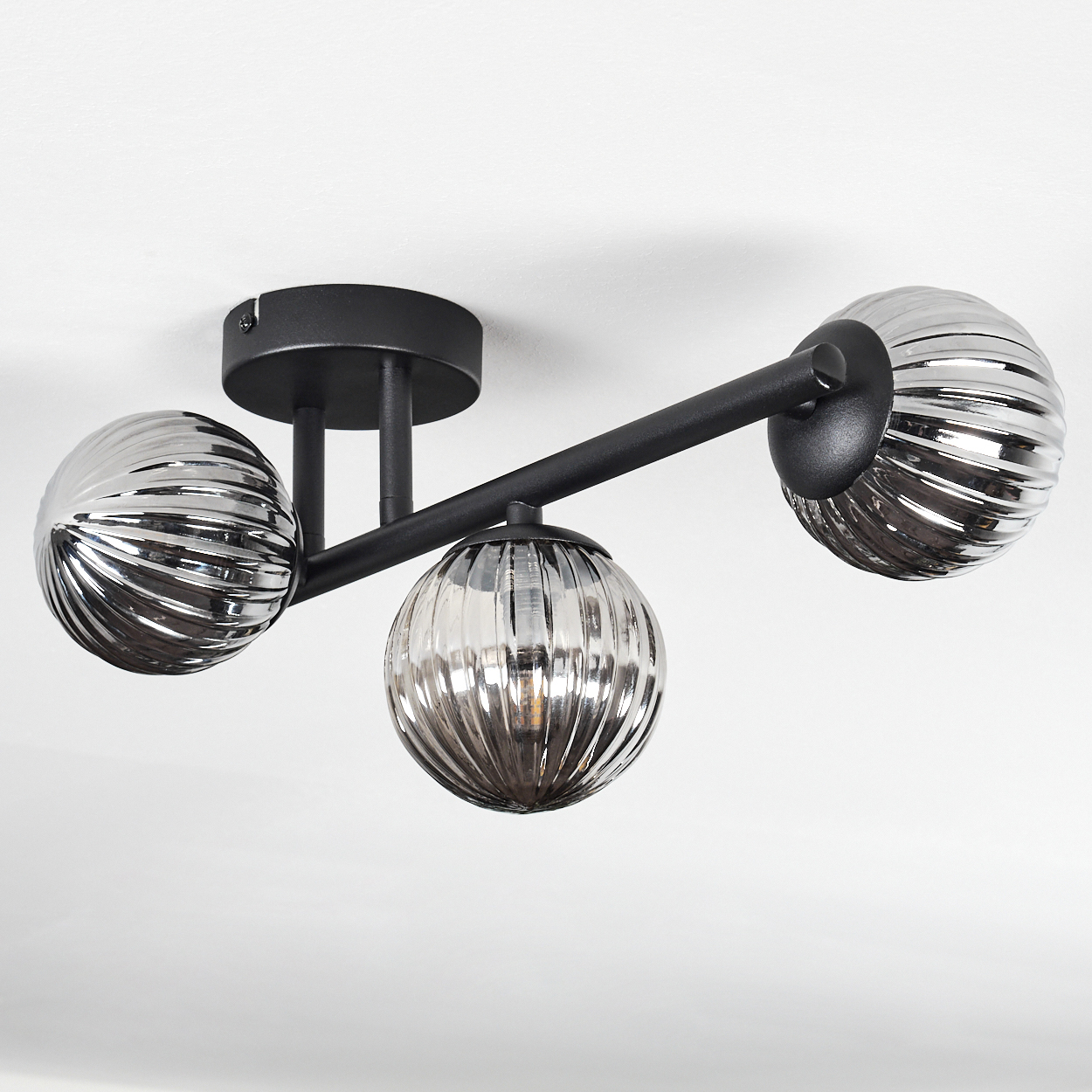 Eine moderne Deckenleuchte mit drei kugelförmigen Lampen. Die Lampen sind silber und geriffelt, befestigt an einem schwarzen Metallrahmen.