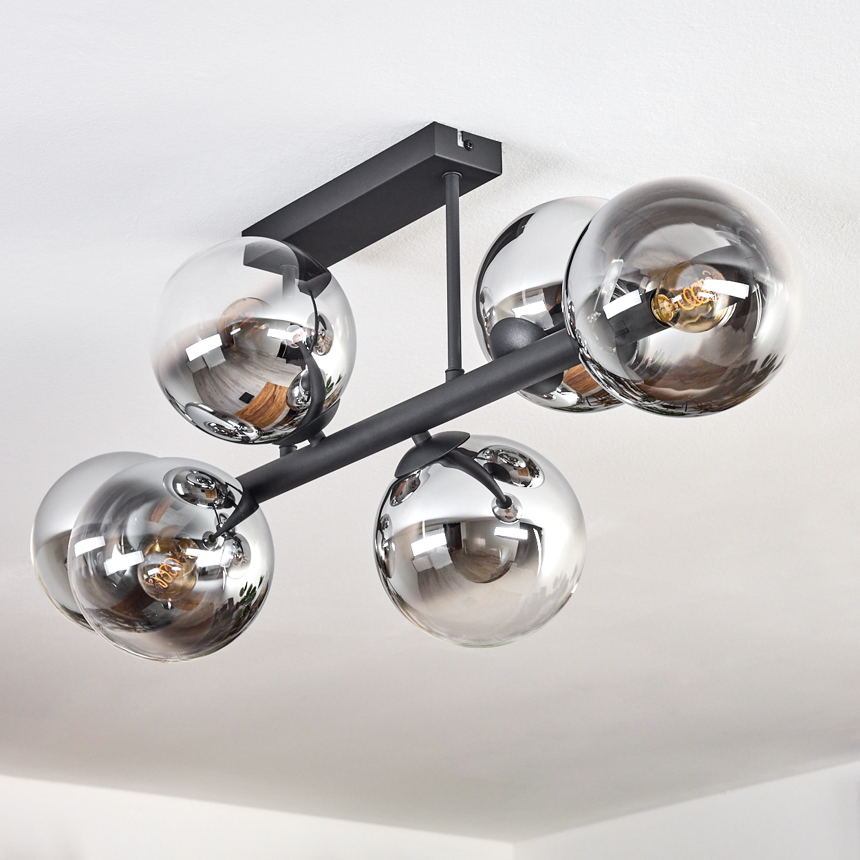 Eine moderne Deckenleuchte mit fünf kugelförmigen, verspiegelten Glasschirmen, schwarzen Metallarmen und einem schwarzen rechteckigen Sockel, vor einer weißen Decke.