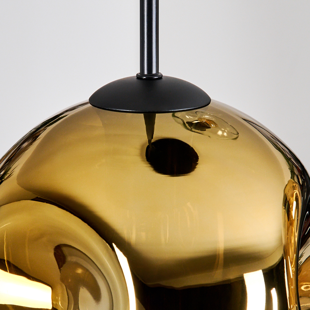 Eine moderne, goldfarbene Glas-Pendelleuchte mit schwarzem Stiel und Kappe hängt vor weißem Hintergrund.