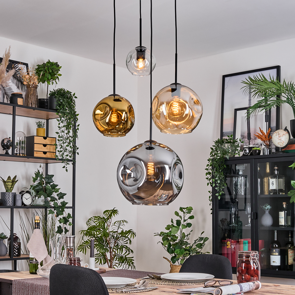 Esszimmer mit hängenden Kugelleuchten. Tisch mit Tellern und Stühlen. Regale mit Pflanzen und Dekor.