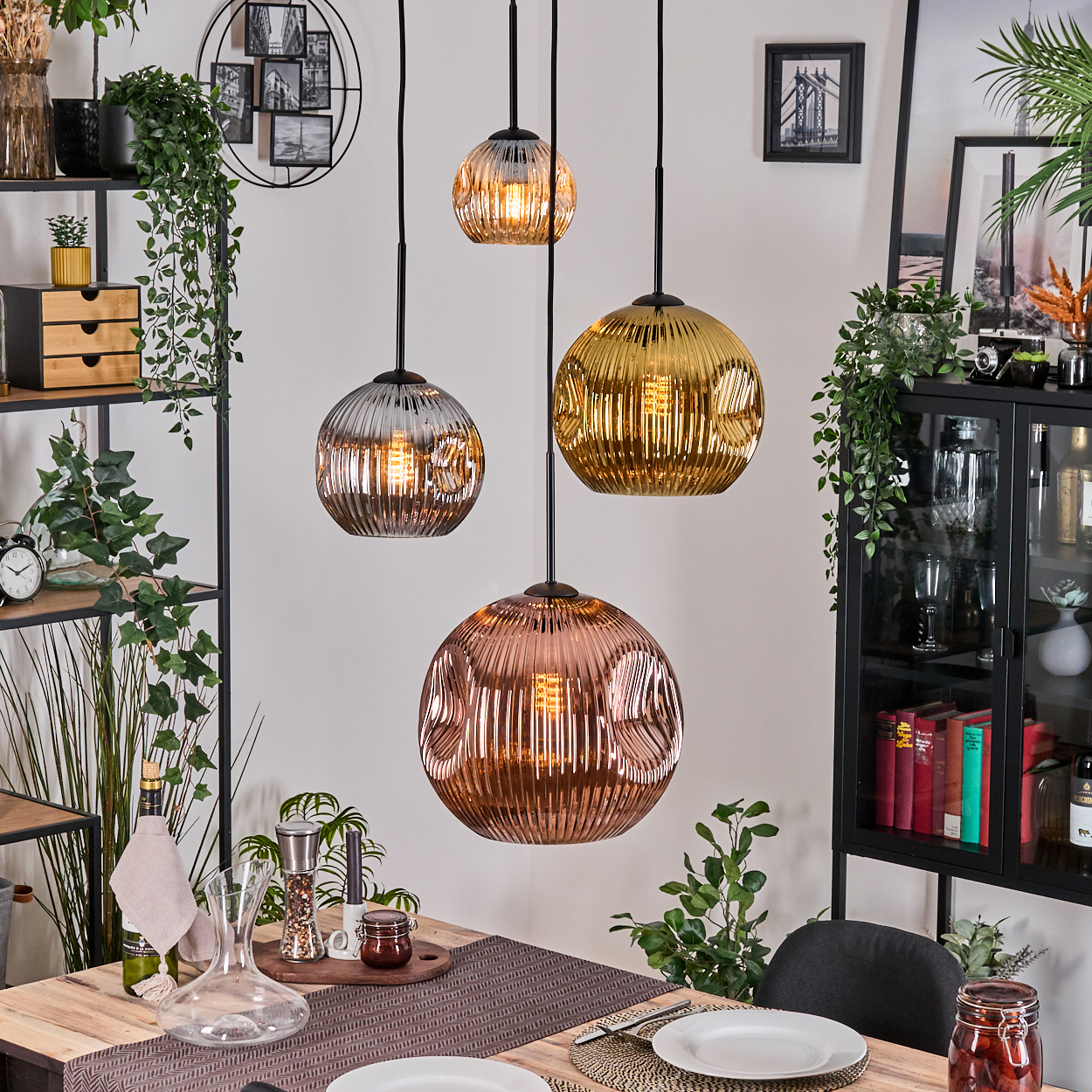 Esszimmer mit vier Hängelampen. Tisch zum Abendessen gedeckt mit Tellern, Kerzen und Pflanzen.