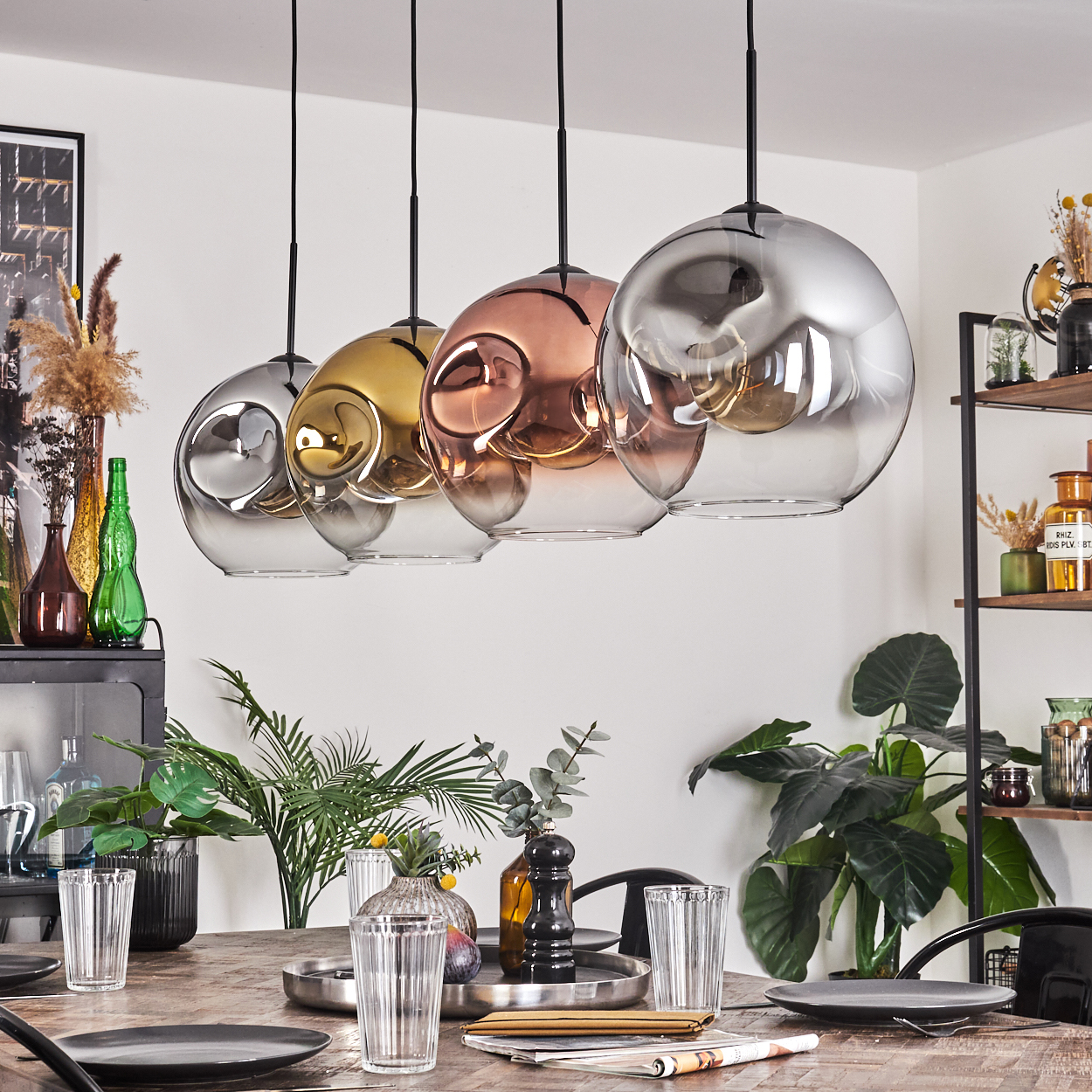 Esszimmer mit vier Glaskronleuchtern. Ein Holztisch ist mit Tellern und Gläsern gedeckt. Pflanzen und Dekor befinden sich im Hintergrund.