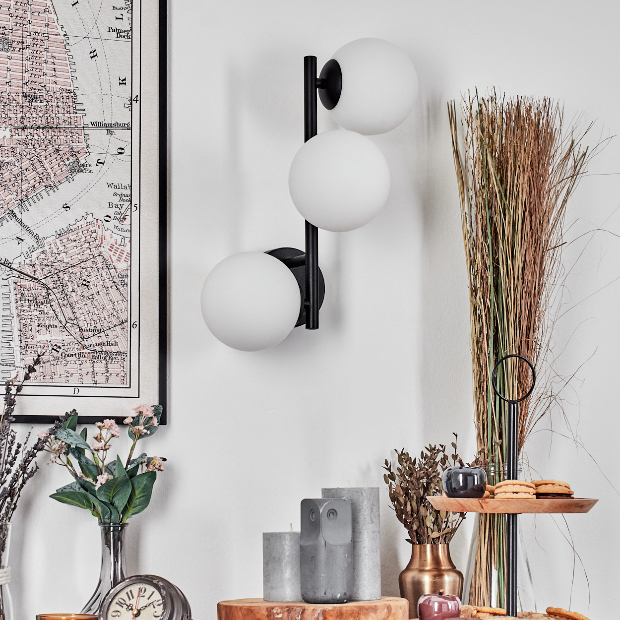 Eine moderne Innenszene mit Wandlampe, Karte, Blumen, Kerzen und Dekorationsartikeln auf einer Holzoberfläche.