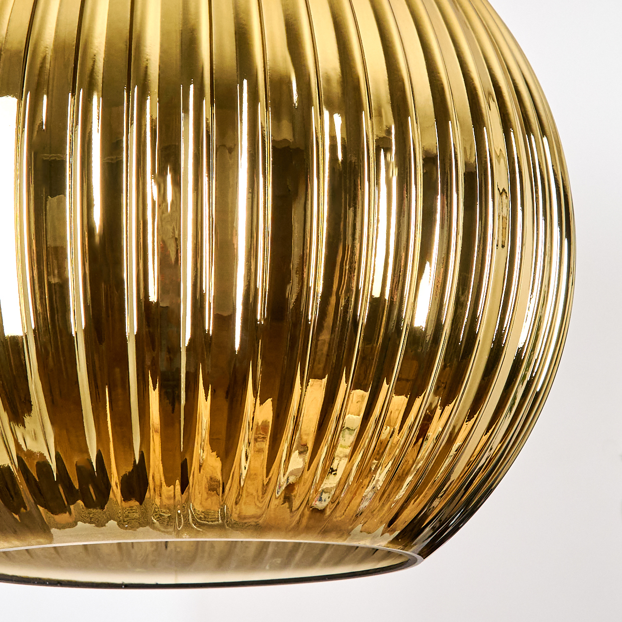 Nahaufnahme eines goldenen, gerippten Glasobjekts vor weißem Hintergrund. Das Glas reflektiert das Licht.