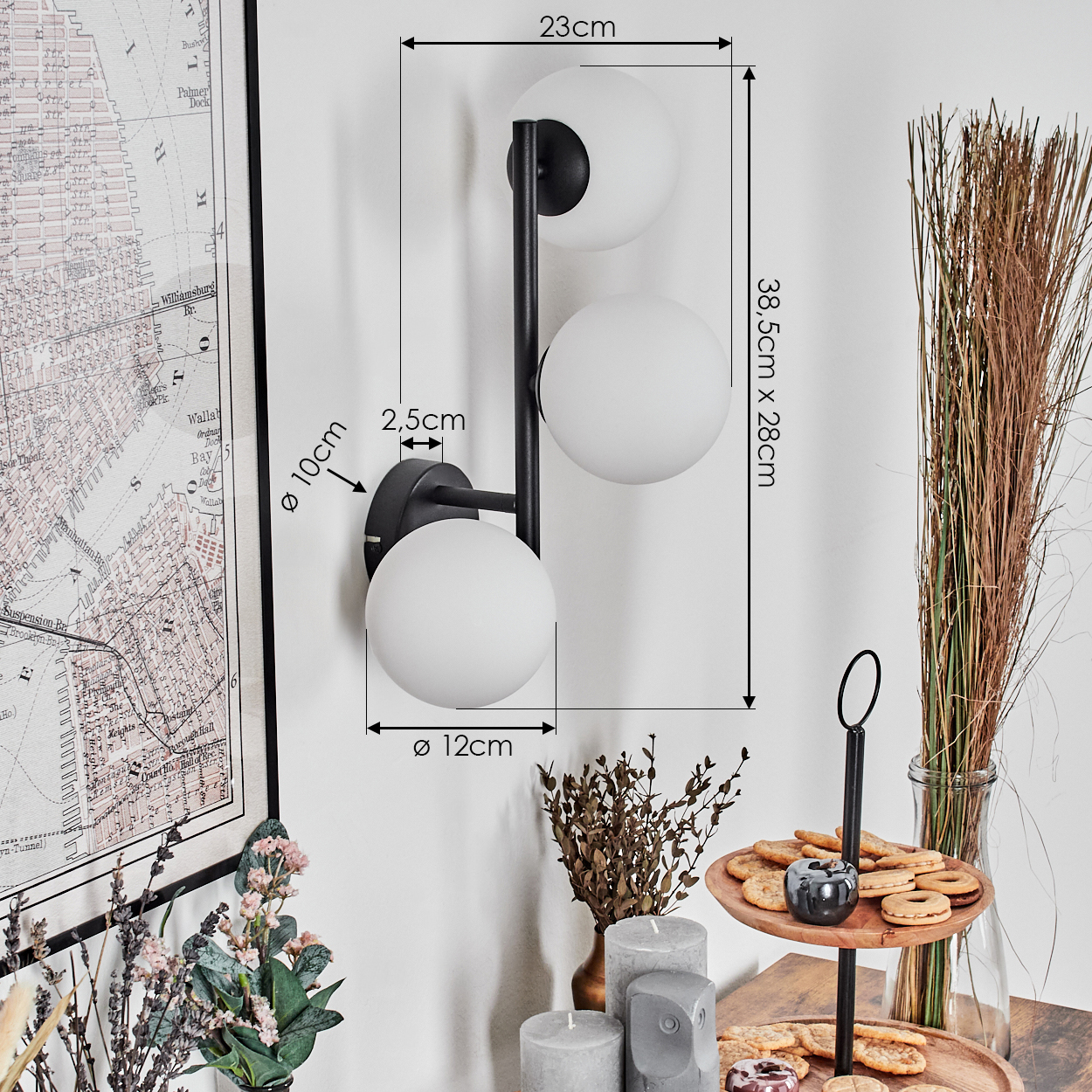Eine moderne schwarze Wandlampe mit drei weißen Kugelleuchten. Eine Karte, Blumen, Kerzen und Kekse sind ebenfalls sichtbar.