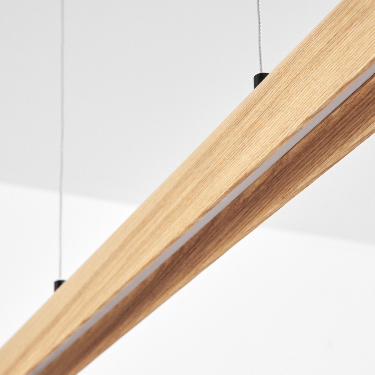 Nahaufnahme eines Holzbalkens mit integriertem Licht, der von der Decke hängt. Der Hintergrund ist eine weiße Decke.