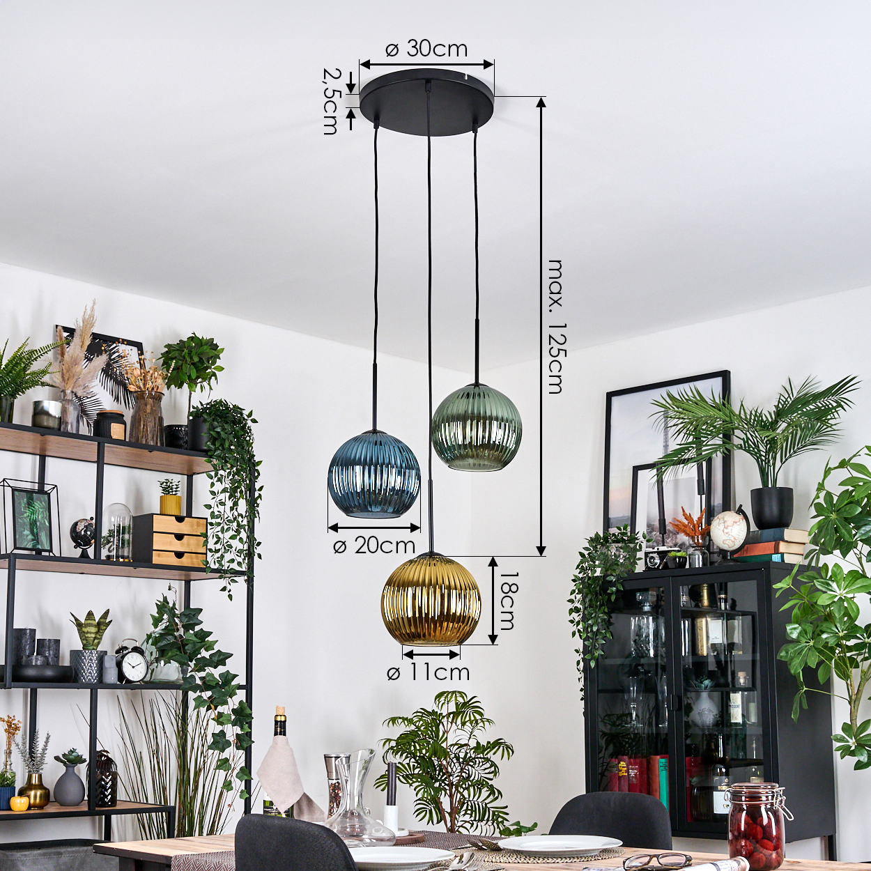 Drei Pendelleuchten mit Glaskugeln, blau, grün und gold, hängen von der Decke. Ein Esszimmer mit Pflanzen, Regalen und einem Tisch.