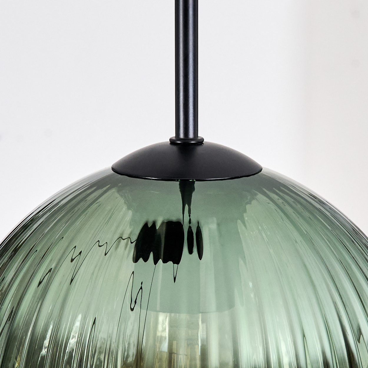 Nahaufnahme einer grünen, gerippten Glas-Hängeleuchte mit schwarzen Metallakzenten vor weißem Hintergrund.